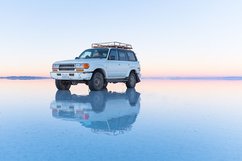 Bil speglar sig i vattnet på Salar de Uyuni..