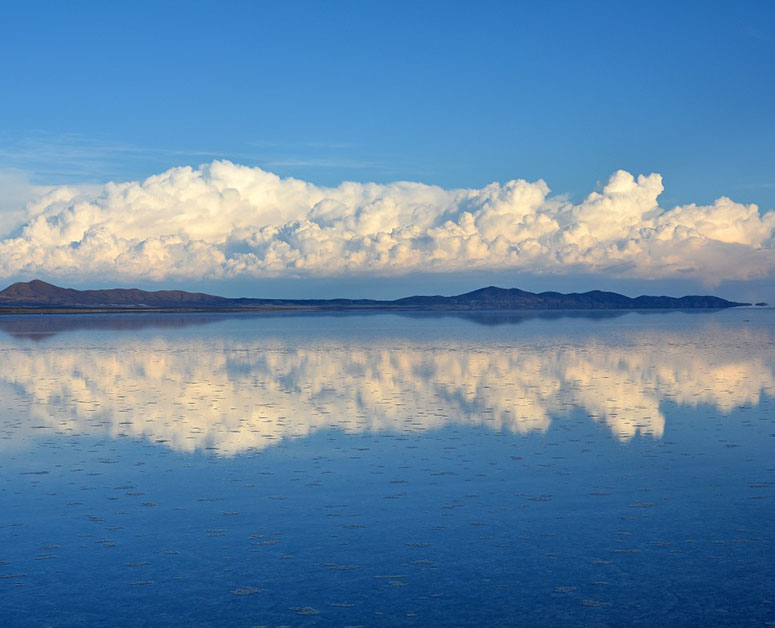 Moln och berg speglar sig i Salar de Uyuni..