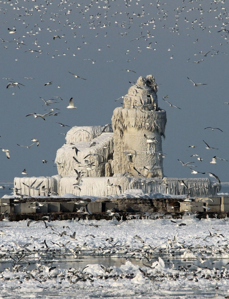 Fyrtorn täckt av is i Cleveland, USA, med fåglar flygandes omkring.