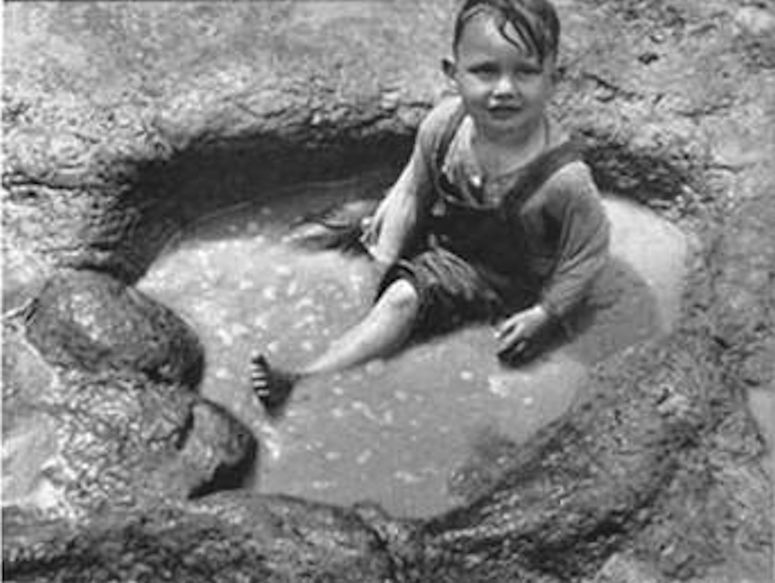 Ett barn badar i ett fossilt fotspår från en dinosaurie