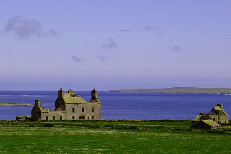 Ett gammalt hus p Westray, med Papa Westray i bakgrunden. Dr emellan gr vrldens kortaste reguljra flygtur.