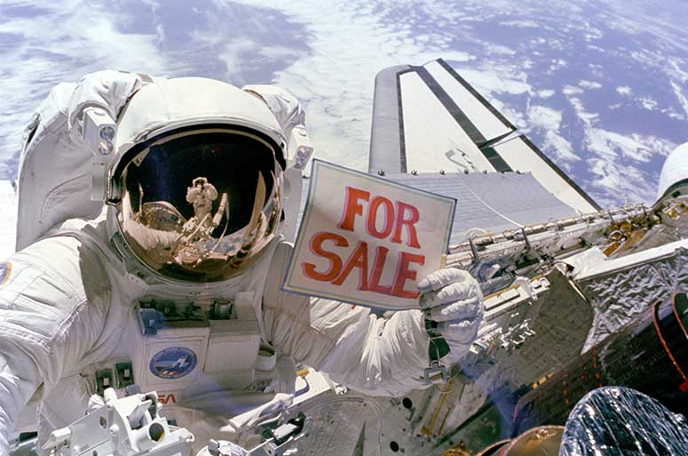 Astronaut Dale A. Gardner håller upp en skylt som det står For Sale på, i rymden.